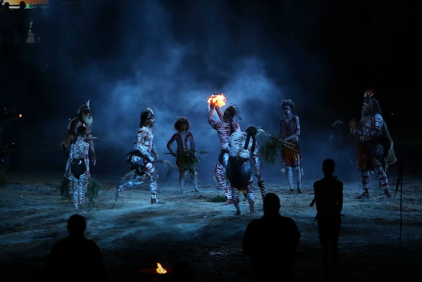 An Indigenous dancer holds a flame while others dance around him in a smoking ceremony