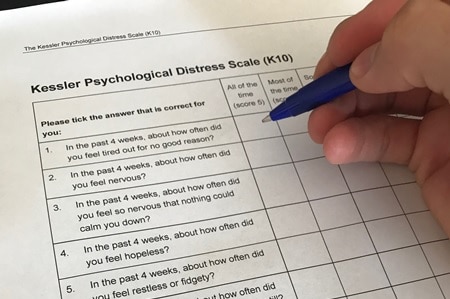 Hand poised to fill in the K10 questionnaire in story about anxiety around getting a mental health plan