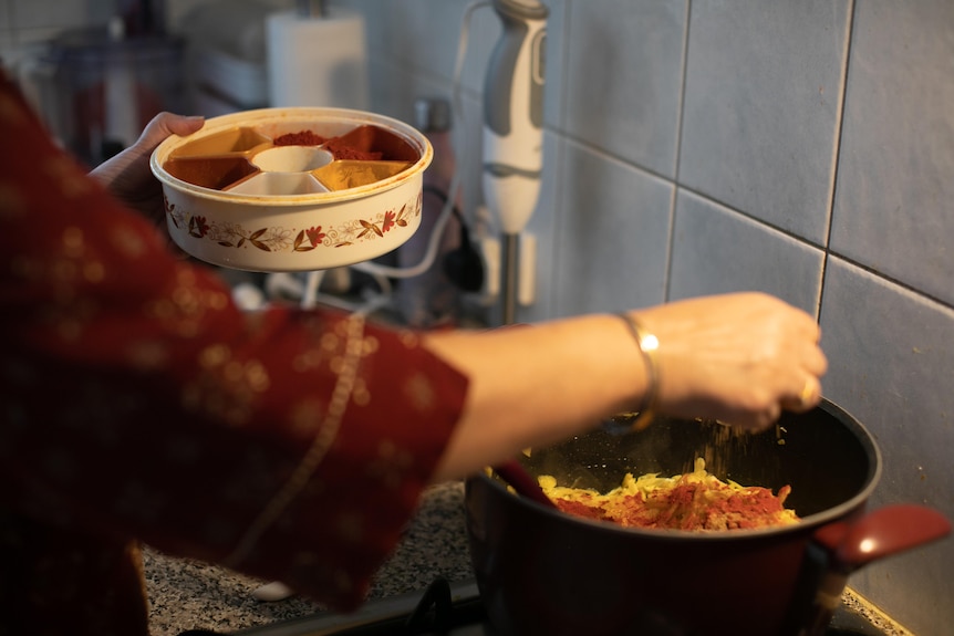 A woman's hand holding a round box full of spices as she adds spices to dish with other hand.