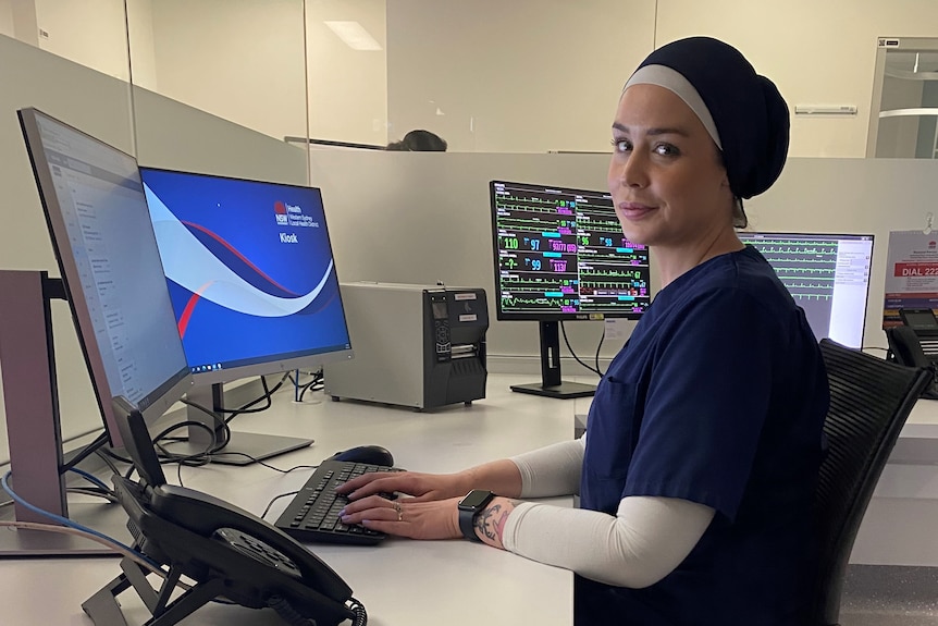 A nurse sits in front of computer screens at a work station in a hospital. 