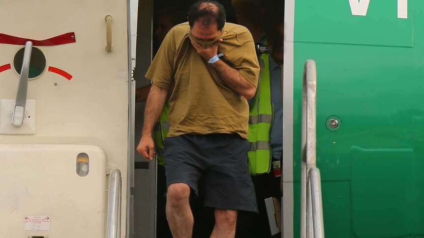 An asylum seeker covers his face as he leaves a plane on Manus Island