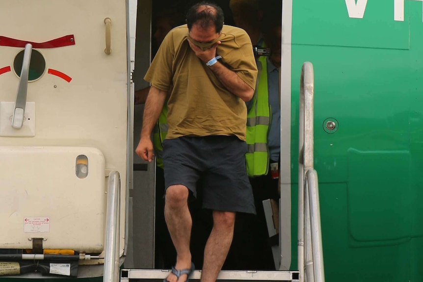 An asylum seeker covers his face as he leaves a plane on Manus Island