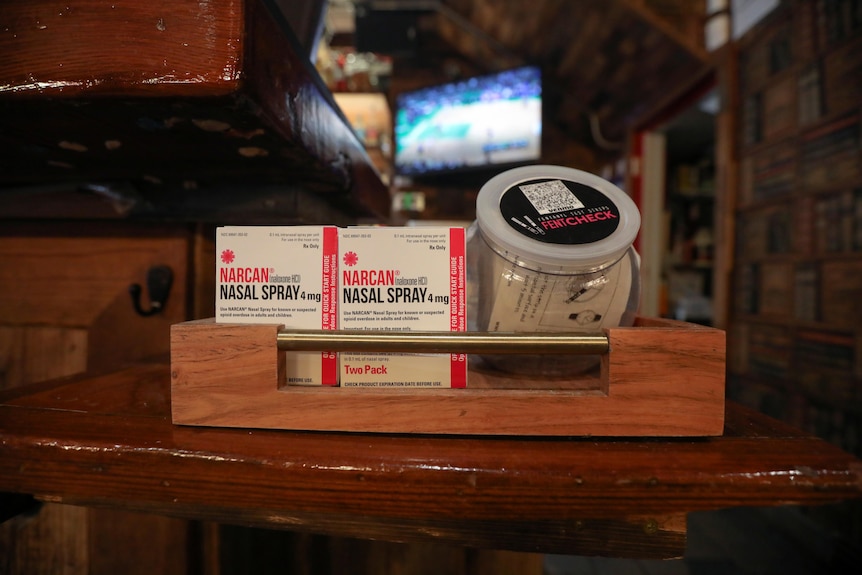 A wooden tray with two boxes containing Narcan nasal spay and fentanyl test strips in a bar