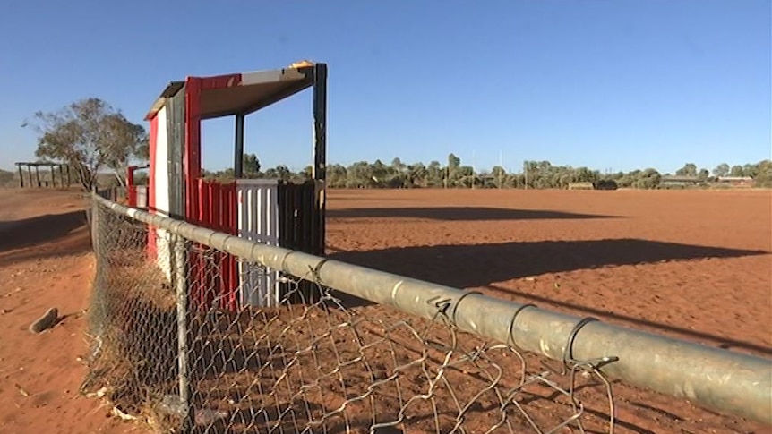 A boundary fence meets the red, black and white interchange bench at the Ltyentye Apurte Football Club at a dirt oval.