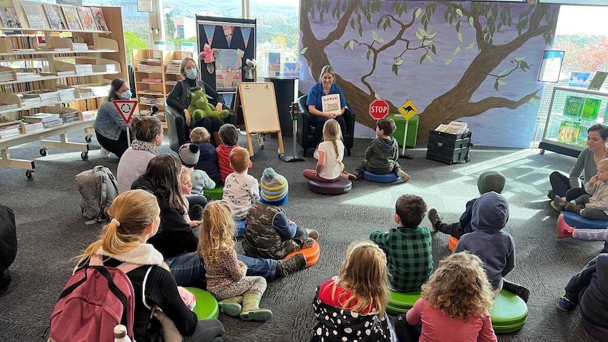 lots of young children sitting on the floor at a library listening to a story about road safety.