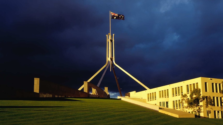 Dark blue storm clouds gather behind the iconic flag poll at Australia's Federal Parliament