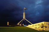 Dark blue storm clouds gather behind the iconic flag poll at Australia's Federal Parliament
