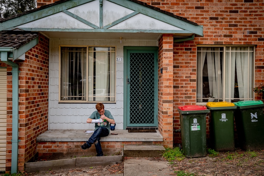 A young man sitting next to the bins smoking.