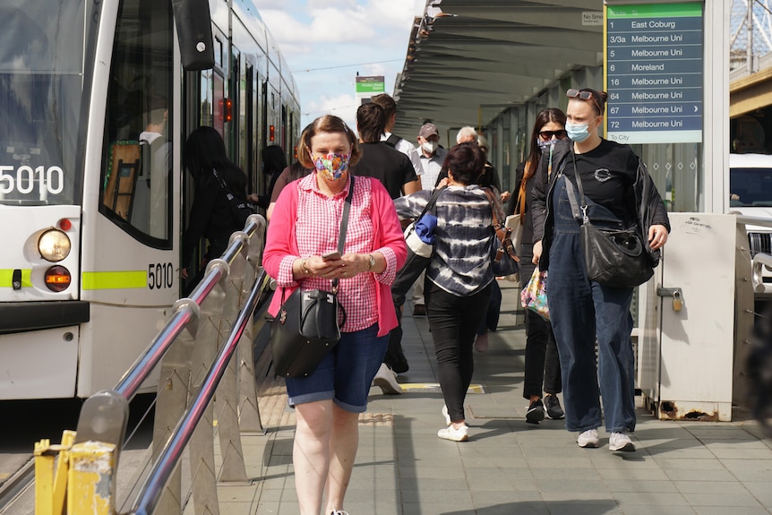 Commuters wear face masks as they walk off a Melbourne tram on a sunny day.
