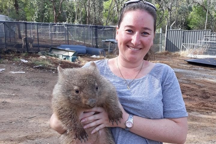 image of woman in grey shirt with sunglasses holding small wombat