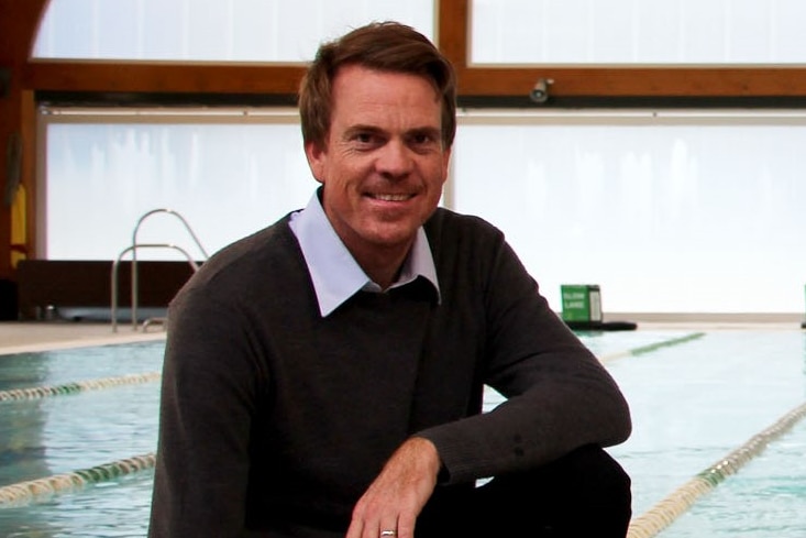 A man crouched by a pool with a child all smiling 
