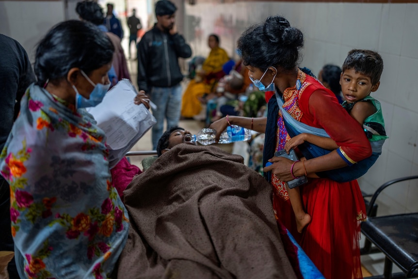 A woman pours water into the mouth of a person on a stretcher in a hospital in Ambikapur