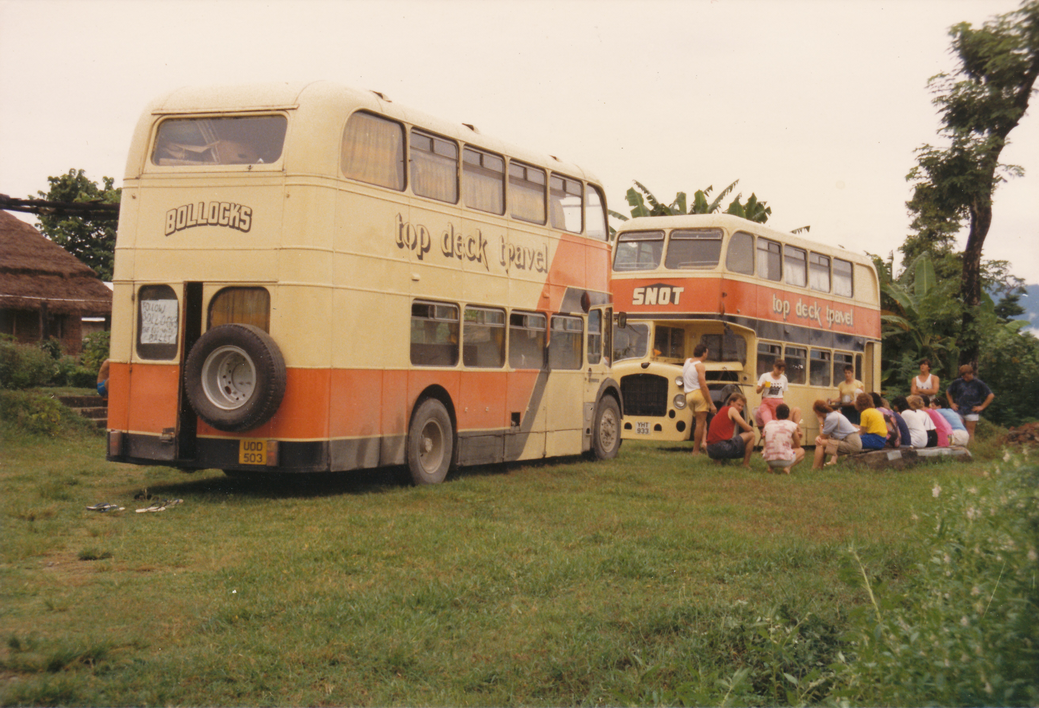 two large busses with tourists sitting around it 