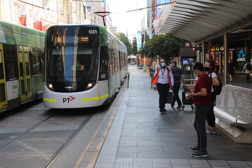 People wait for a Melbourne tram on Bourke Street, all wearing masks.