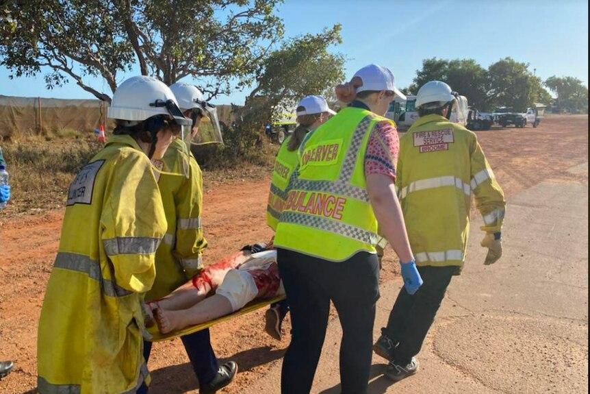 Girls in high vis carry the patient.