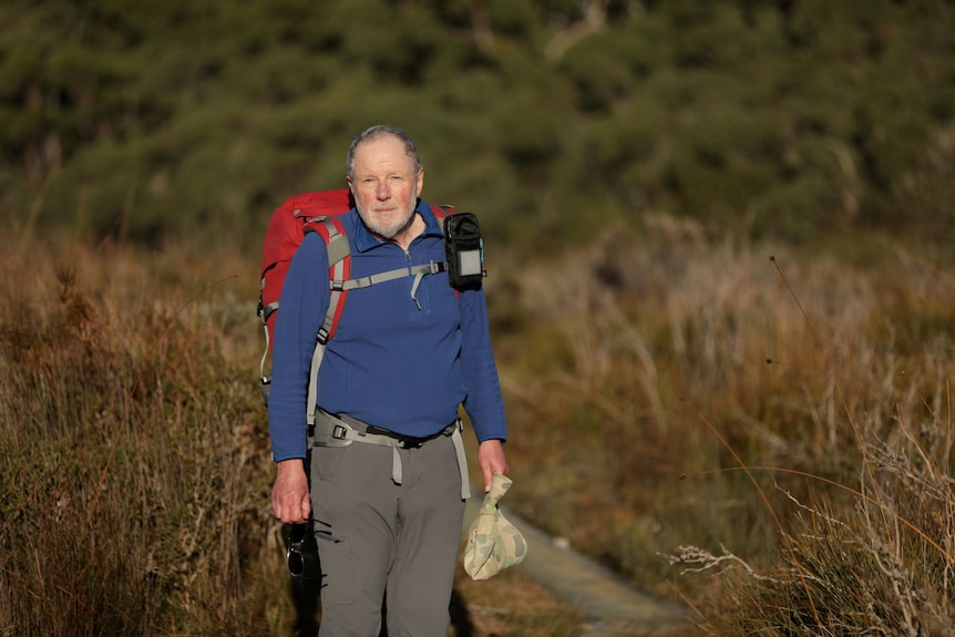 An older man in a blue jumper with backpack in the wilderness