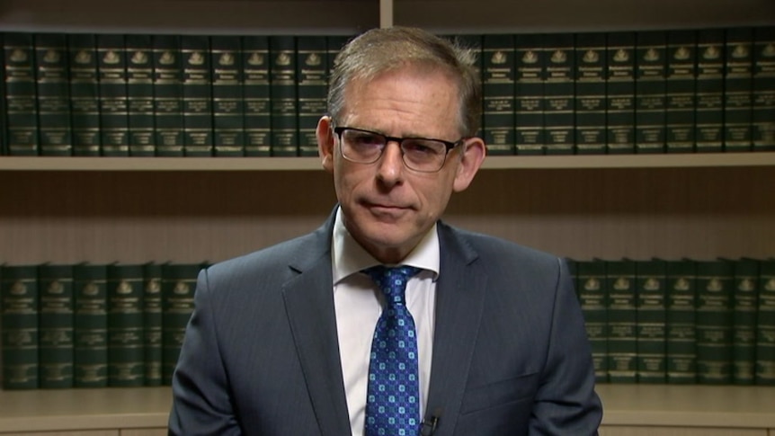 Anthony Byrne stands in front of a bookshelf with green legal books