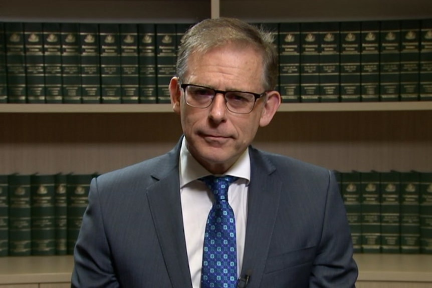 Anthony Byrne stands in front of a bookshelf with green legal books