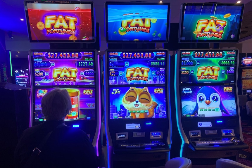 The silhouette of a woman sitting at a colourful pokies machine