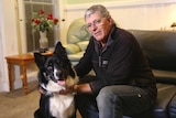 Former pet food operations manager, Dennis Pedretti, sitting in his lounge room patting his dog