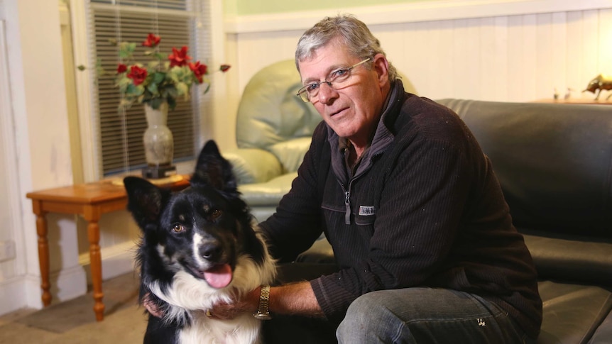 Former pet food operations manager, Dennis Pedretti, sitting in his lounge room patting his dog