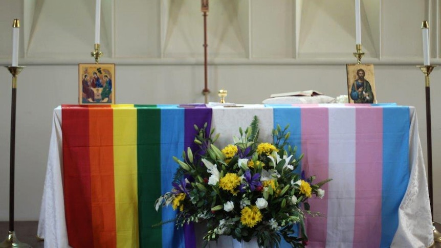Gay and transgender pride flags lie on a table in a church.