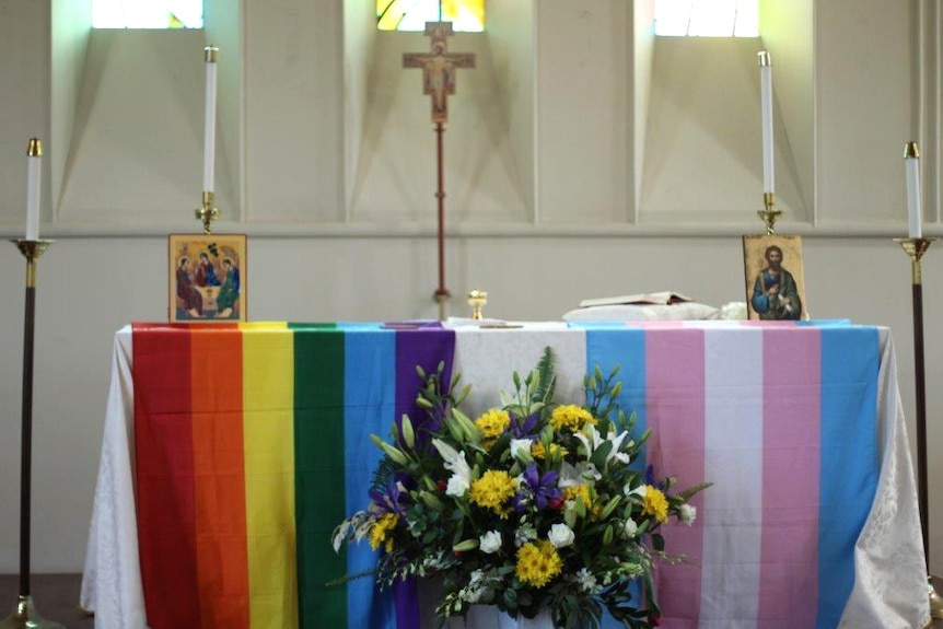 Gay and transgender pride flags lie on a table in a church.