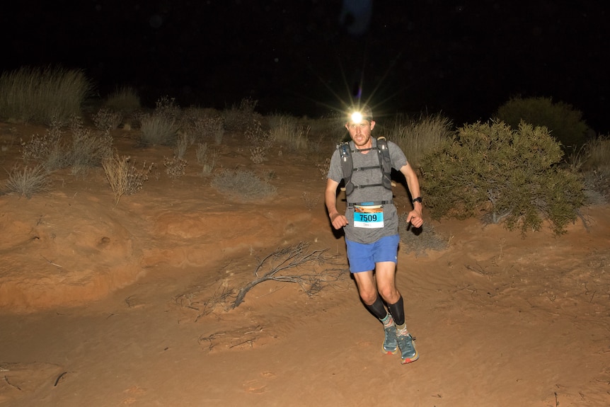 A runner with a headlamp runs through the dark, night time, desert terrain.
