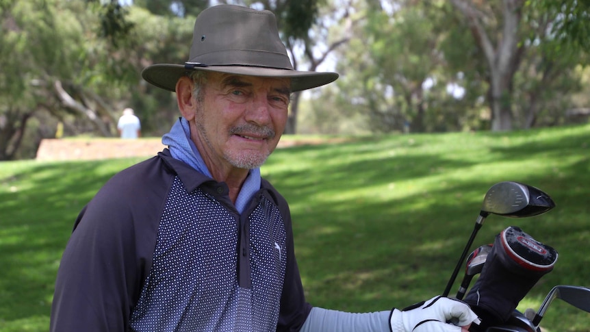 A man in a hat with gold clubs and a golf course in the background.