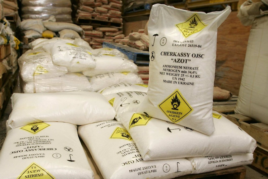 Several white bags sit on a crate. The bags sat ammonium nitrate and have yellow warning symbols on them.