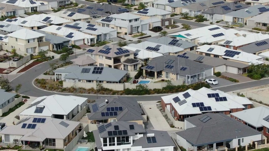 An aerial view of a suburb, many of whose houses have solar panels.