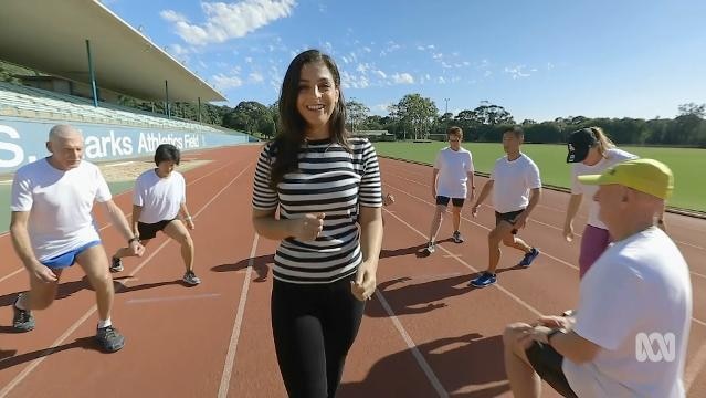 A woman surrounded by elderly people stretching their legs on a running track