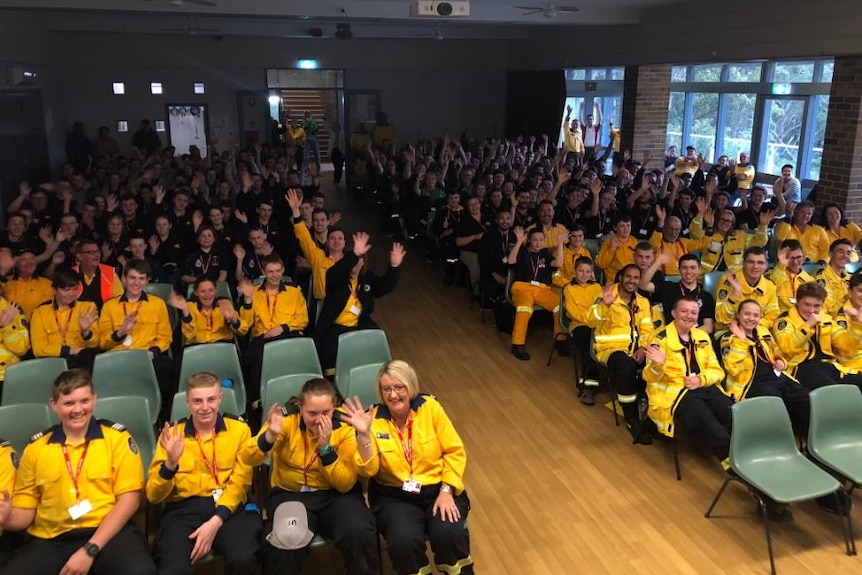 A group of people in yellow uniforms wave in a hall.