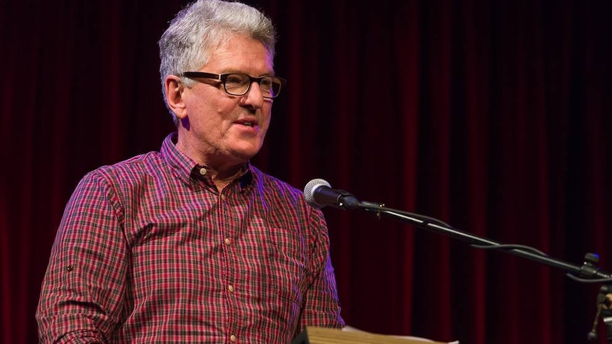 David Marr with grey hair and glasses stands speaking into a microphone.