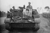 Four men in military uniforms poke their heads out of a tank with a portrait of Indonesian leader Soekrano stuck to the front