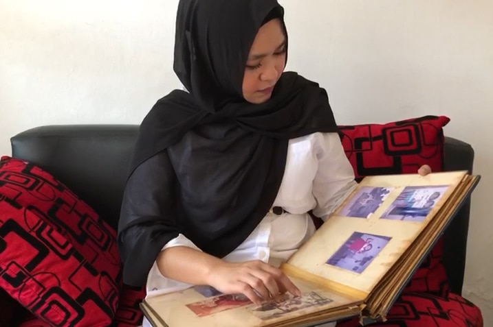 A young woman wearing a hijab flicks through a family photo album.