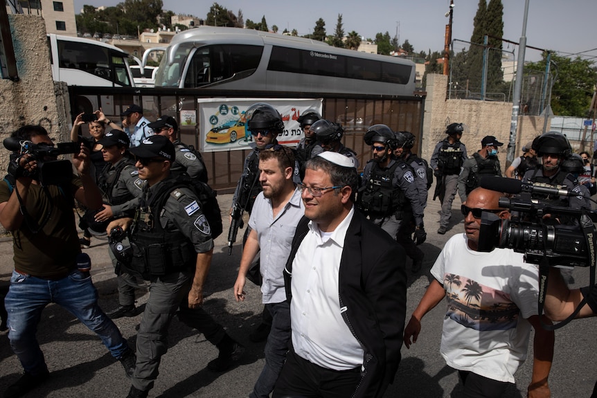 A man in a yarmulke walking down a road surrounded by photographers 