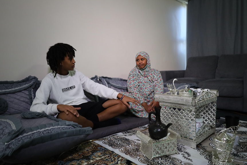 A young man and a woman sit on cushions on the floor of their home