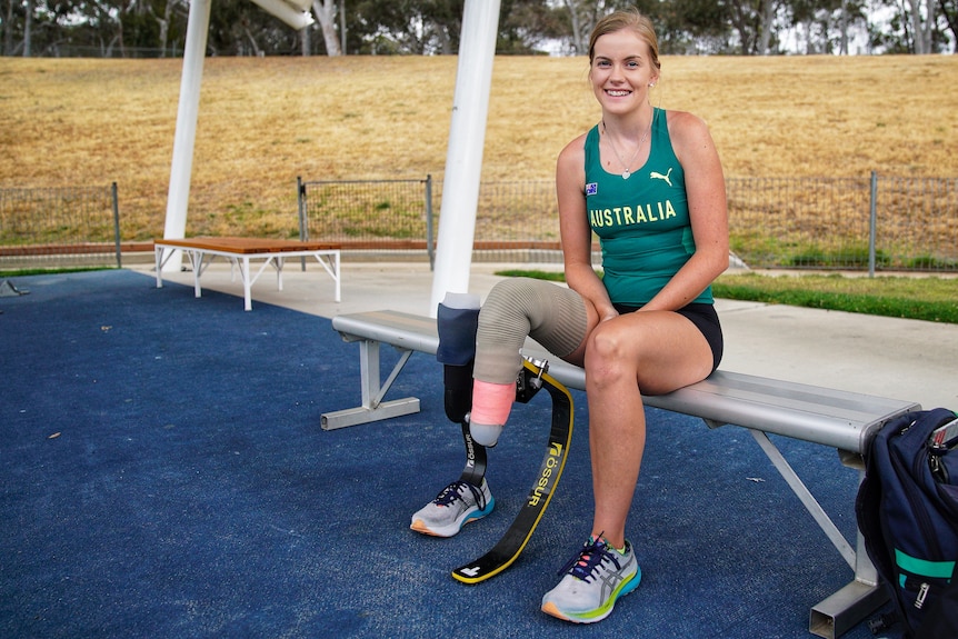 An Australian para-sport athlete sits at a training area wearing a prosthetic right leg and a jumping blade in front of her. 