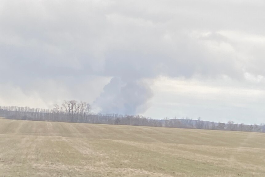 Plume of smoke rising above empty field.