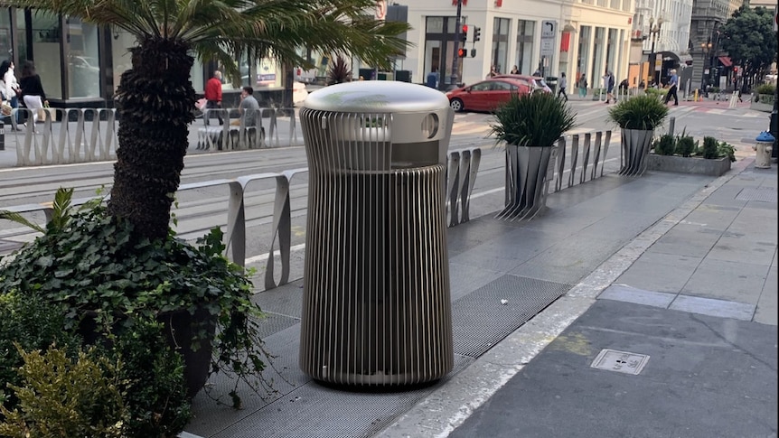 A render of a sleek metal cylindrical street bin is the focus of an image on a tram-lined San Francisco hilly street.