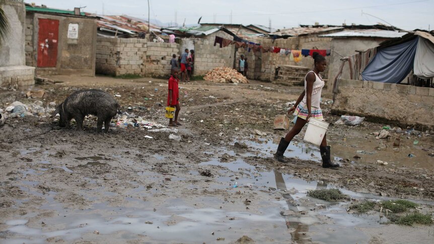 A woman walks through a muddy bog with a bucket.