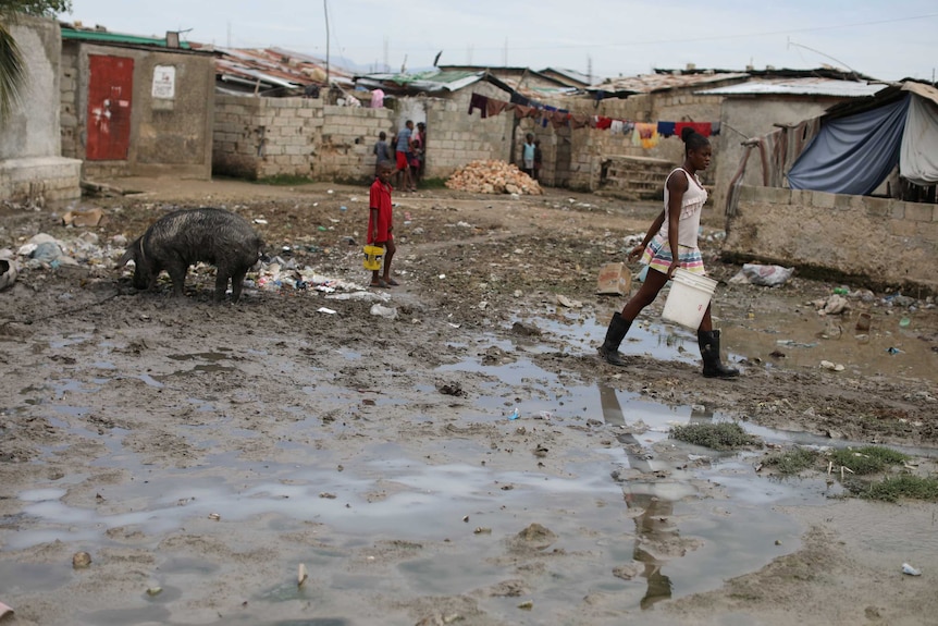 A woman walks through a muddy bog with a bucket.