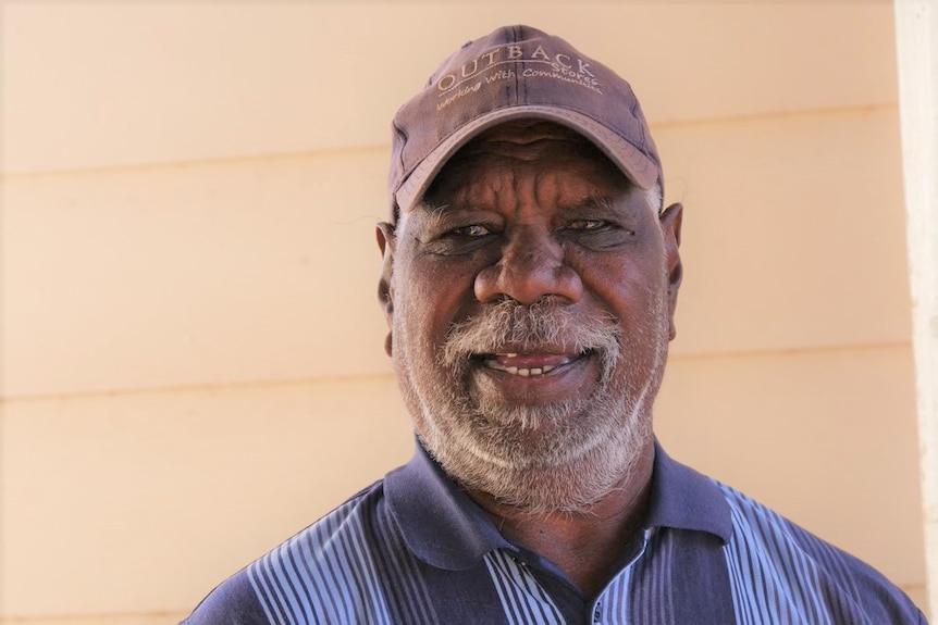 An Aboriginal man wearing a cap smiles at the camera