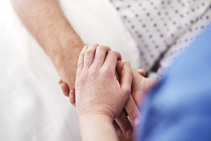 A hand holding the hand of a patient lying in a hospital bed.