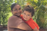 A woman smiles, she is holding a smiling toddler