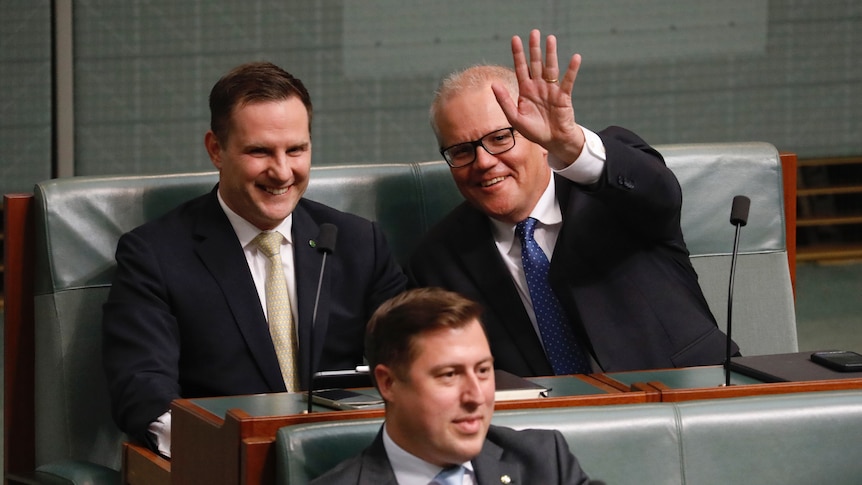 Morrison and Hawke smile as Morrison waves to the camera from the house of representatives backbenches