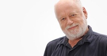 Late Night Live host Phillip Adams poses for a photo against a white backdrop.