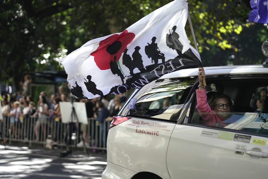 woman in pink waving lest we forget flag out a car window