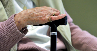 An elderly woman holds a walking stick